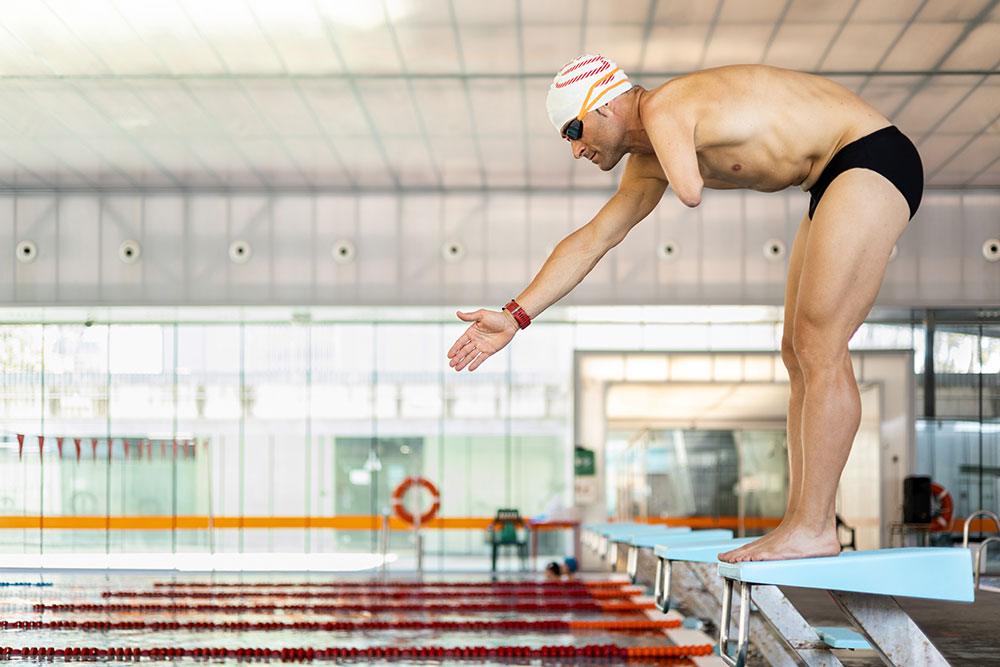 Adult swimmer with an amputated arm is about to jump on the platform of an indoor pool